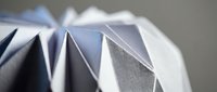 White origami paper sculpture with geometric triangular folds creating dimensional angular patterns on neutral background for modern design projects.