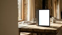 Blank tablet screen on rustic wooden table with coffee cup in warm sunlit room for digital mockup and presentation design.