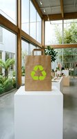 Eco-friendly brown paper shopping bag with green recycling symbol displayed in modern sustainable retail store with natural lighting and plants.