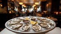 Fresh oysters on ice served on a silver platter with lemon and sauce in an elegant restaurant setting, perfect for seafood menus.