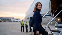 Professional businesswoman in navy suit boarding private jet at sunset airport with ground crew in background for corporate travel and luxury lifestyle.