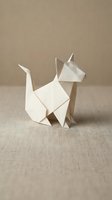 White origami cat figure folded from paper on neutral beige fabric background showcasing Japanese paper folding art and minimalist craft design.