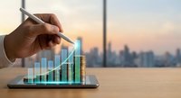 Business growth concept with hand pointing at rising financial chart on tablet screen against urban skyline background at sunset.