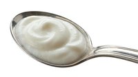Creamy white yogurt or sour cream swirl on metal spoon against white background, suitable for food packaging, recipe blogs, and culinary advertising.