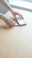 Hands connecting USB cable to smartphone on wooden desk for charging and data transfer in bright modern workspace.