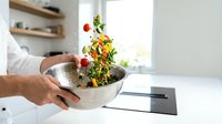 Fresh vegetables falling into stainless steel bowl in modern kitchen. Healthy cooking preparation with colorful ingredients for nutritious meal.