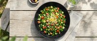 Overhead view of colorful vegetable stir-fry with peas, carrots, and corn in black wok on wooden table, perfect for cooking and food blogs.