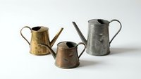Vintage metal watering cans in brass, copper, and silver finishes isolated on white background, ready for design projects and product mockups.