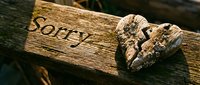 Broken stone heart on a rustic wooden plank with the word Sorry carved in, symbolizing apology, regret, and emotional pain in relationships.