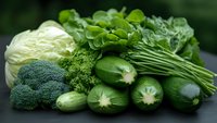 Fresh green vegetables including cabbage, broccoli, cucumbers and leafy greens arranged on dark background, healthy organic produce for nutritious eating.