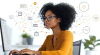 Young African American businesswoman with natural curly hair and glasses working at computer with digital marketing icons and analytics symbols floating around.