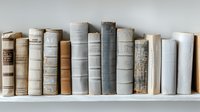 Row of vintage books in neutral tones arranged on white shelf against light wall, creating minimalist aesthetic for home decor and interior design styling.