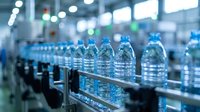 Plastic water bottles moving along conveyor belt in modern beverage manufacturing facility with blurred industrial background and production equipment.