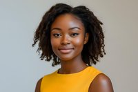 Young African American woman with natural curly hair wearing yellow sleeveless top smiling confidently against neutral background. Professional headshot style portrait.