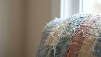 Colorful textured fabric with frayed edges in soft pastel tones creates artistic surface detail for interior design and craft projects.