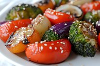 Grilled colorful vegetables with sesame seeds on white plate, featuring cherry tomatoes, broccoli, mushrooms and red onion in Asian-inspired marinade.