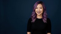 Young Asian woman with purple hair smiling confidently in black top against dark background for professional headshot and portrait photography.