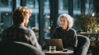 Mature businesswoman with gray hair smiling during meeting with colleague in modern office. Professional consultation and corporate teamwork concept.