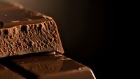 Rich dark chocolate bar pieces with aerated texture on black background, perfect for culinary and confectionery marketing materials.