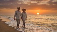 Senior couple walking hand in hand on beach at golden sunset, romantic vacation moment with ocean waves and warm sky colors creating peaceful atmosphere.