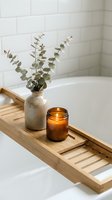 Spa bathroom setup with eucalyptus branches in ceramic vase, lit amber candle on wooden bathtub caddy, white subway tile backdrop, relaxation and wellness decor.