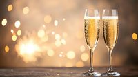 Two elegant champagne flutes filled with sparkling wine against blurred golden bokeh lights background, creating romantic festive atmosphere for celebration.