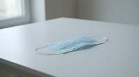 Surgical face mask with elastic ear loops lying on white surface in bright indoor setting, suitable for healthcare, medical, and safety-related projects.