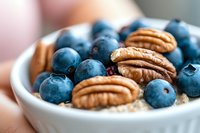 Fresh blueberries and pecan nuts in white bowl with oatmeal porridge, healthy breakfast macro photography with selective focus and bokeh background.