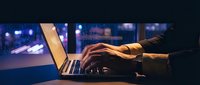 Professional working late at night on laptop computer in modern office with city lights background creating productive workspace atmosphere.