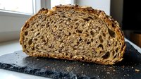 Artisan multigrain bread loaf with seeds and nuts on dark slate board, rustic bakery product for healthy eating and organic food concepts.