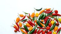 Colorful hot chili peppers collection with red, orange, yellow and green varieties scattered on white background for culinary and cooking designs.