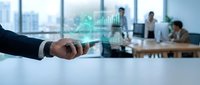 Businessman hand holding holographic digital graph projection in modern office with colleagues working in background for data analysis presentations.