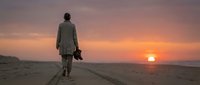 Man in casual clothing walking alone on empty desert road at sunset, holding shoes in hand, contemplative journey and solitude concept for travel and lifestyle projects.