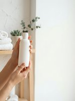 Woman with medium skin tone holding blank white cosmetic bottle for skincare, beauty, or wellness product branding and packaging mockup in bright bathroom setting.