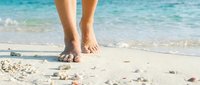 Woman walking barefoot on tropical beach with turquoise ocean waves and white sand. Summer vacation relaxation and wellness concept for travel destinations.