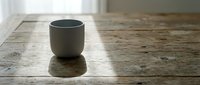Minimalist ceramic cup on wooden surface with natural sunlight casting shadow, suitable for home decor, lifestyle, and product photography projects.
