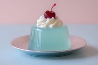 Light blue gelatin dessert topped with whipped cream and a cherry on a pink plate, pastel background, sweet treat concept.