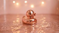 Luxurious rose gold rubber duck floating in sparkling water with warm bokeh lights creating elegant bathroom spa atmosphere for relaxation concepts.