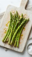 Fresh green asparagus spears with sea salt and lemon zest on rustic wooden cutting board, ready for healthy cooking and gourmet meal preparation.