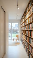 Modern home library with floor-to-ceiling wooden bookshelves, minimalist chair and pendant lighting for reading corner interior design.