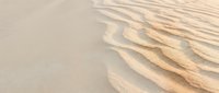 Soft sand waves create natural ripple patterns on a beach shoreline, ideal for travel, nature, and coastal design projects.