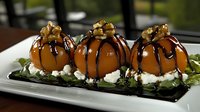 Gourmet dessert spheres with caramel coating, chocolate drizzle and candied nuts served on cream base and dark plate garnished with fresh herbs. Elegant plating.