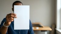 Man holding blank white paper sheet covering face in office environment for mockup and branding purposes.