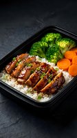 Healthy meal prep container with glazed chicken, steamed broccoli, carrots and rice on dark background for balanced nutrition and diet planning.