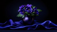 Vibrant purple anemone flowers in dark vase against dramatic black background with flowing blue silk fabric creating elegant mood for fine art photography.