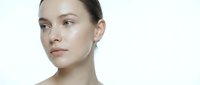 Young Caucasian woman with natural makeup and glowing skin looking sideways on white background for skincare and beauty advertising campaigns.