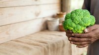 Fresh green broccoli held in hands against rustic wooden background, suitable for healthy eating, organic food, nutrition, and farm-to-table cooking content.