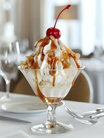 Vanilla ice cream sundae with caramel sauce and cherry topping served in elegant glass bowl at upscale restaurant table setting for dessert menu photography.