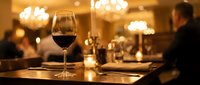 Glass of red wine on elegant restaurant table with warm ambient lighting and blurred diners in luxurious dining room background.