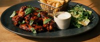 Grilled chicken wings with fresh herbs and creamy dip served on dark plate with salad and bread basket for restaurant menu and food photography.